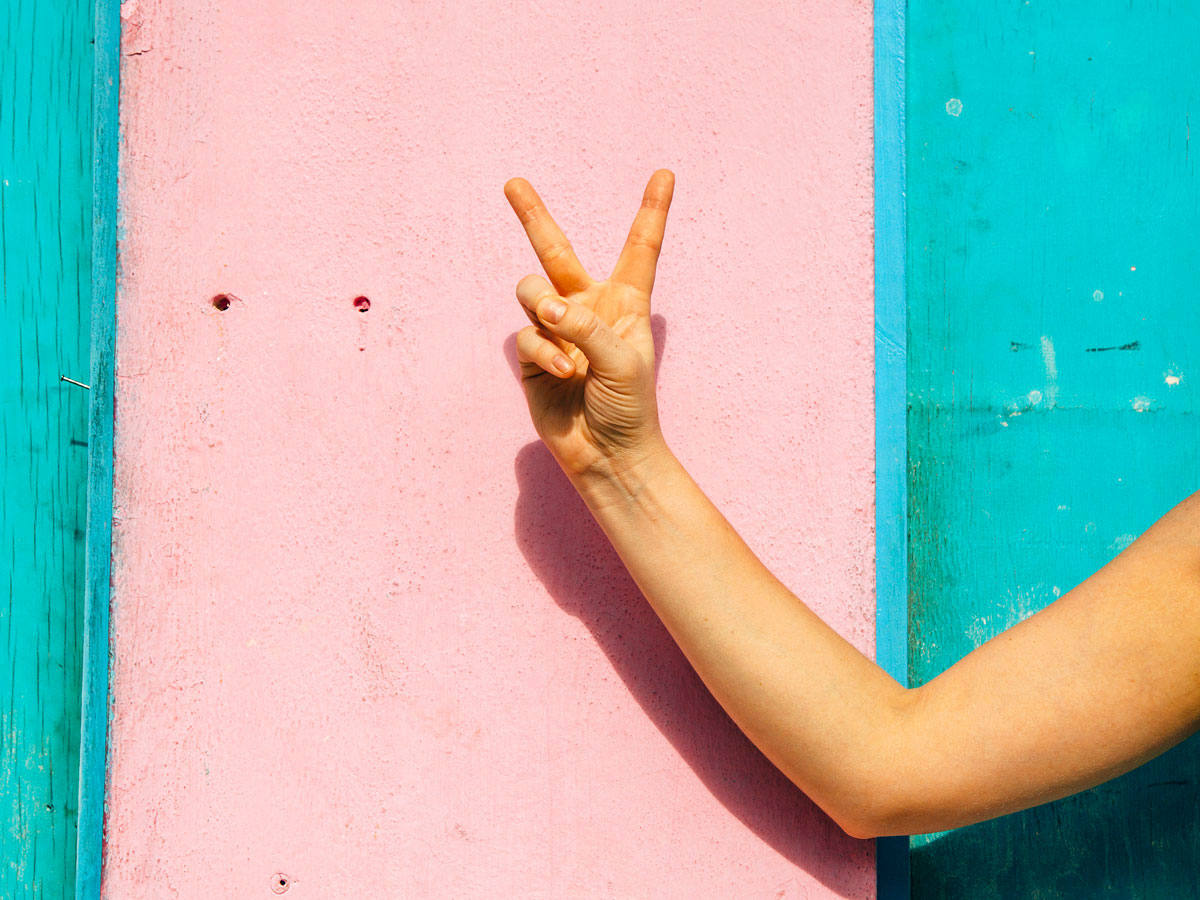 Person giving peace sign against pink wall