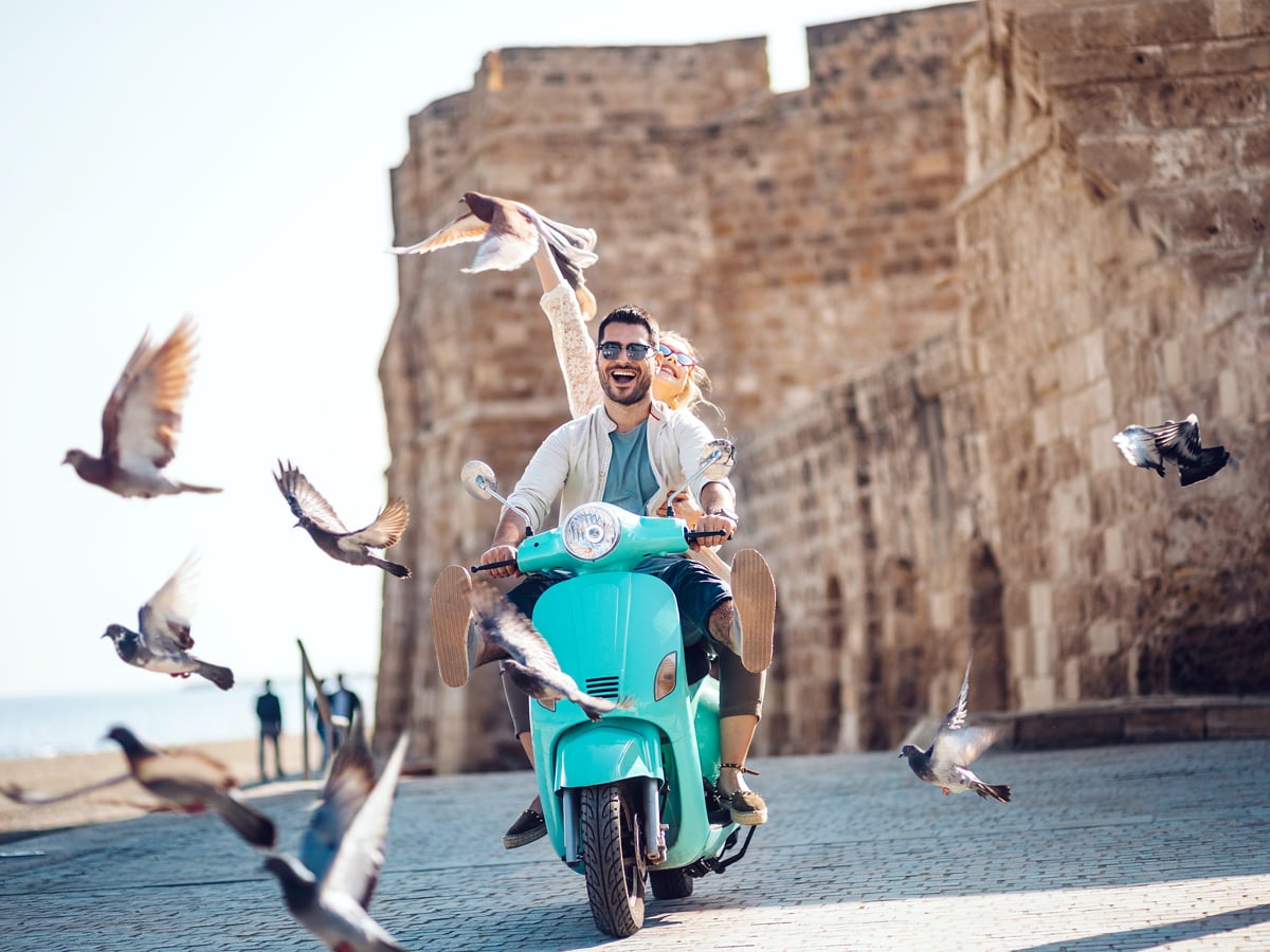 Birds flying in front of tourist couple on Vespa