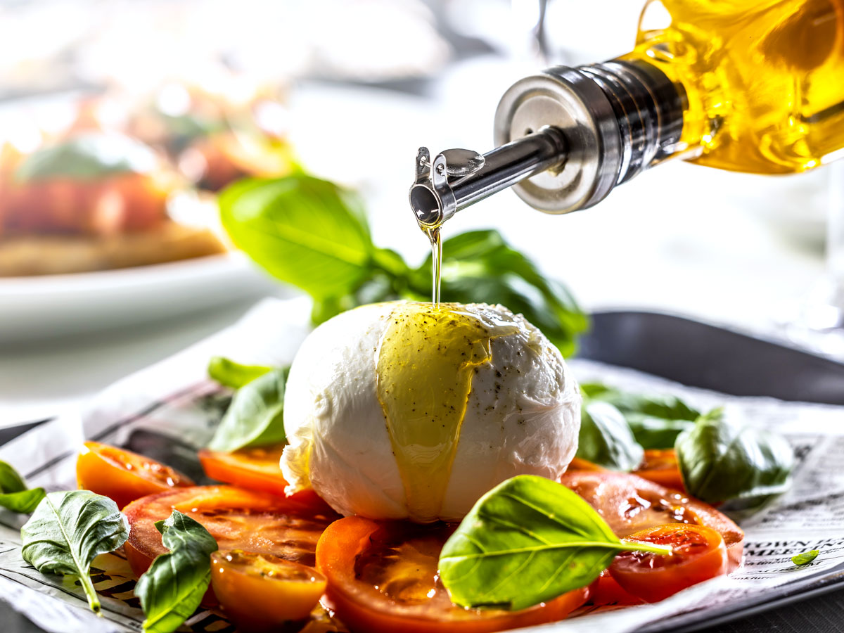 Person drizzling olive oil on caprese salad