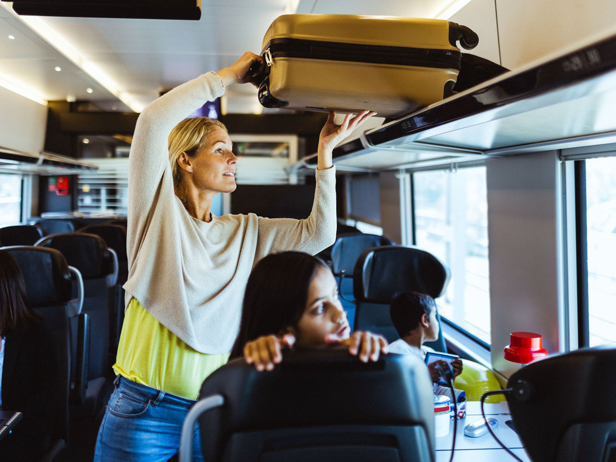 Woman stowing bag above seats on train