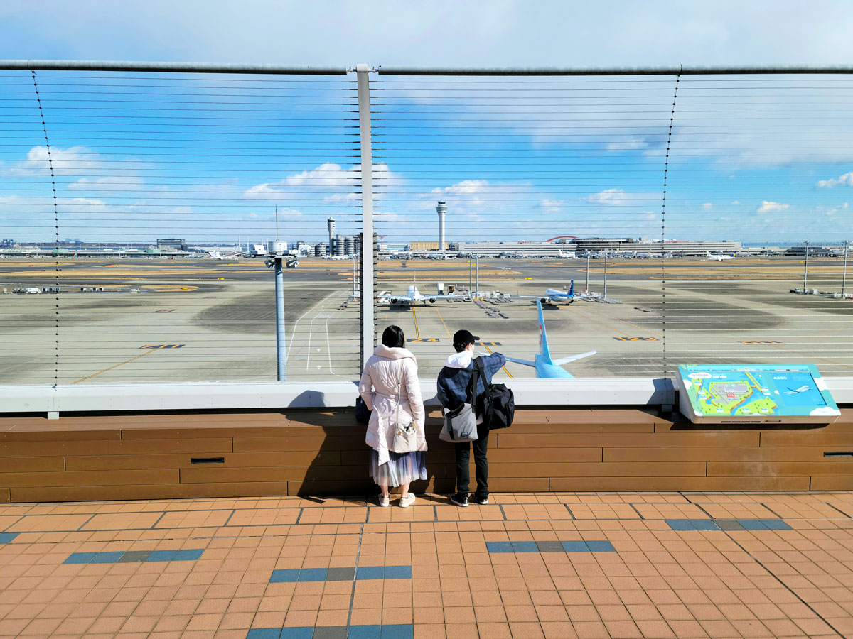 Two people observing planes from observation deck at Tokyo Haneda Airport in Japan