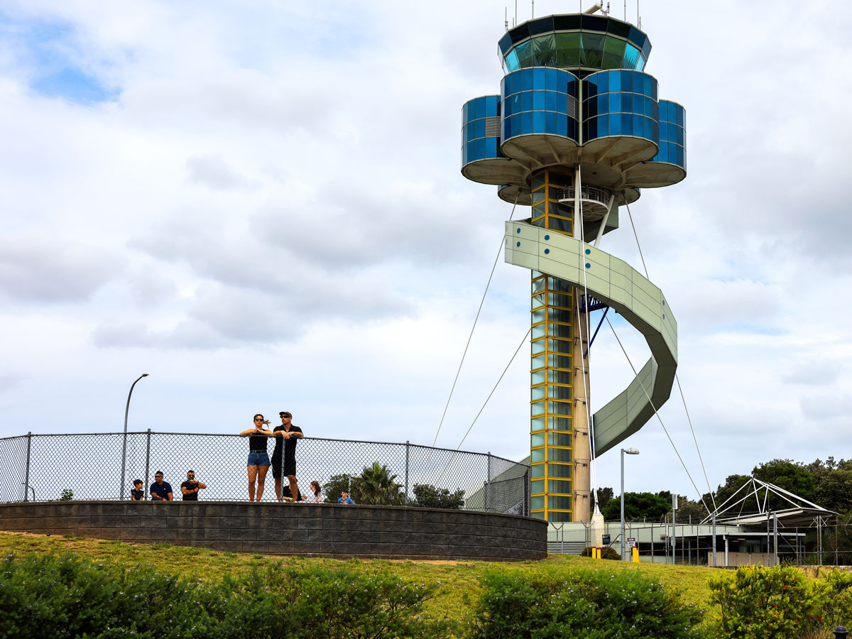 Enthusiasts wathcing planes under the control tower at Sydney Airport, Australia