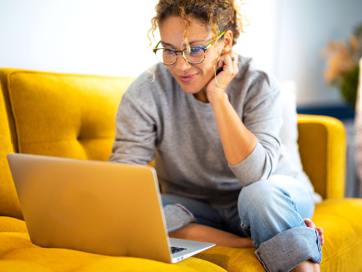 Woman sitting on yellow couch using laptop computer