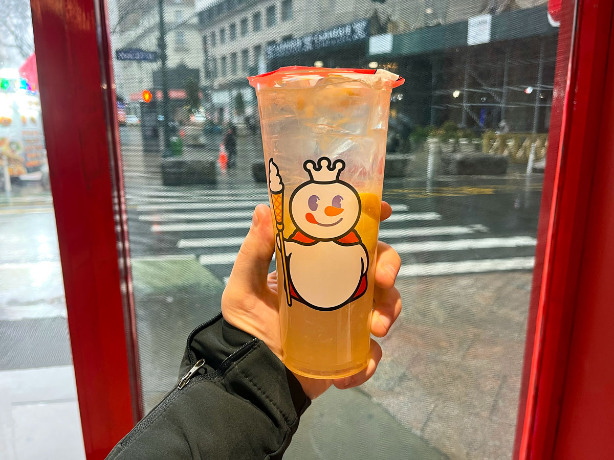 Author holding iced Mixue beverage in front of store window