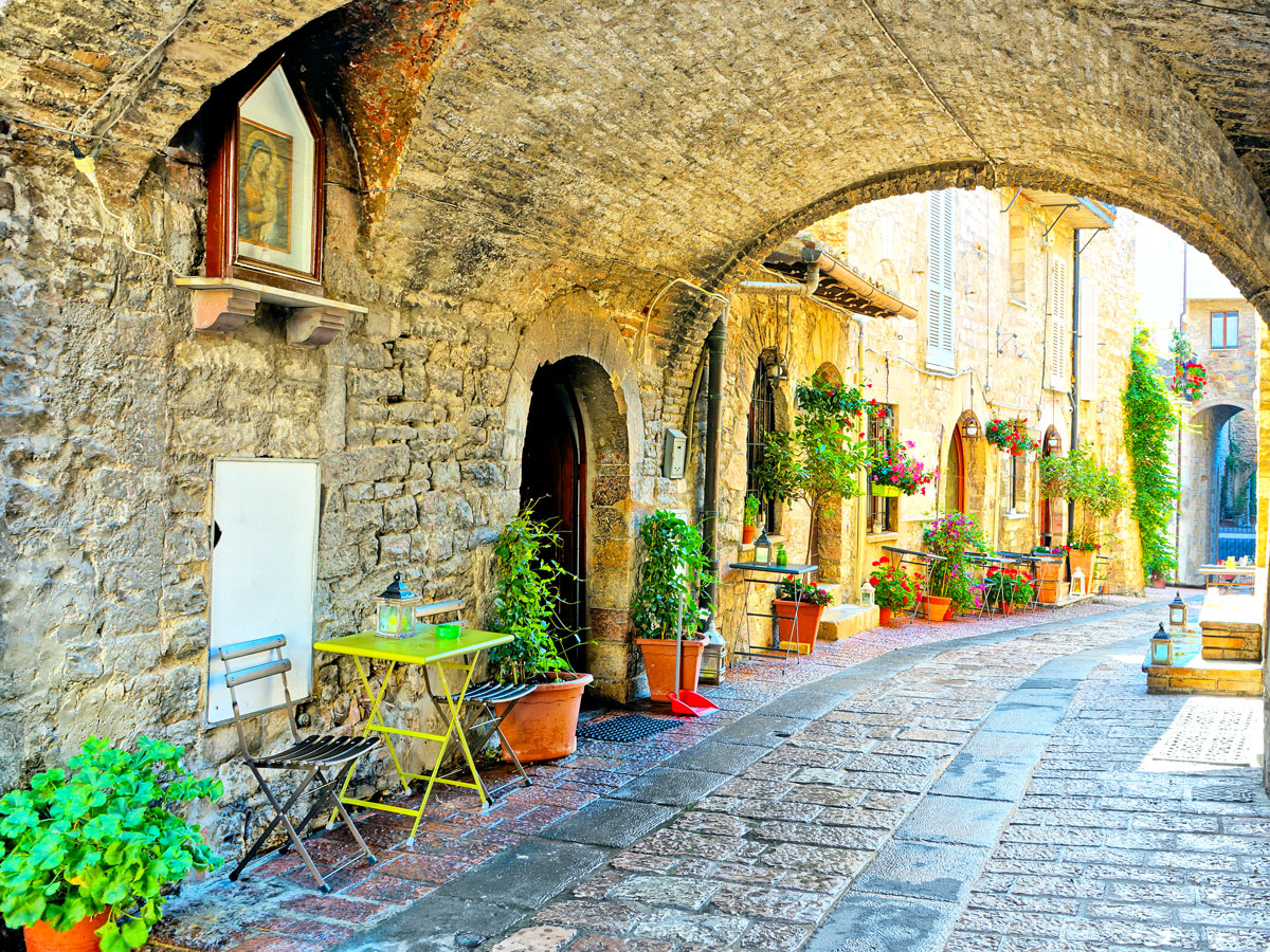 Empty dining tables under stone archway in Assisi, Italy