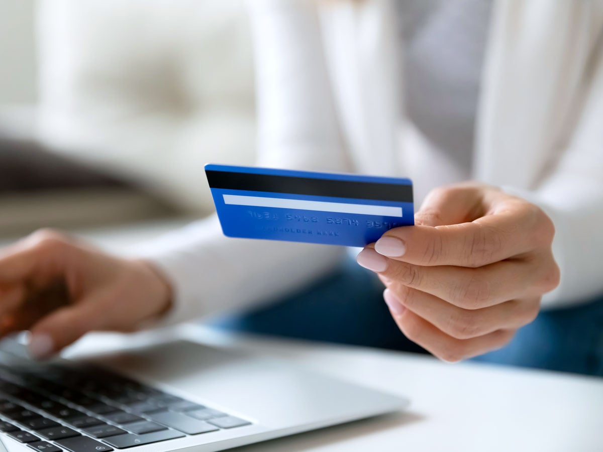 Person holding credit card while typing on laptop