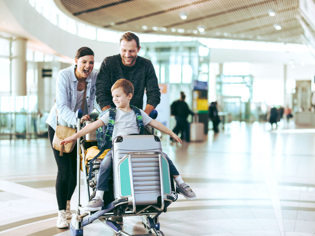 Parents rolling their son on luggage cart through airport