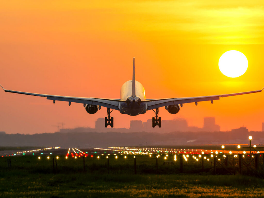 Airplane landing on runway at sunset, with runway lights illuminated