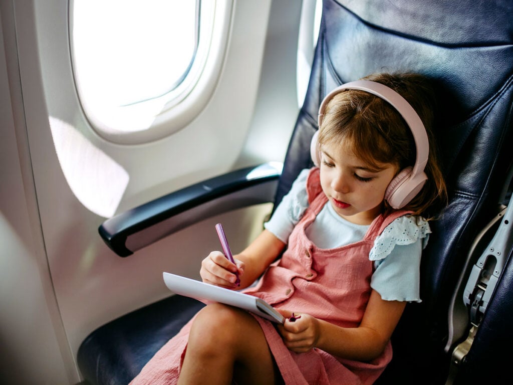 Young child in airplane seat drawing on notepad