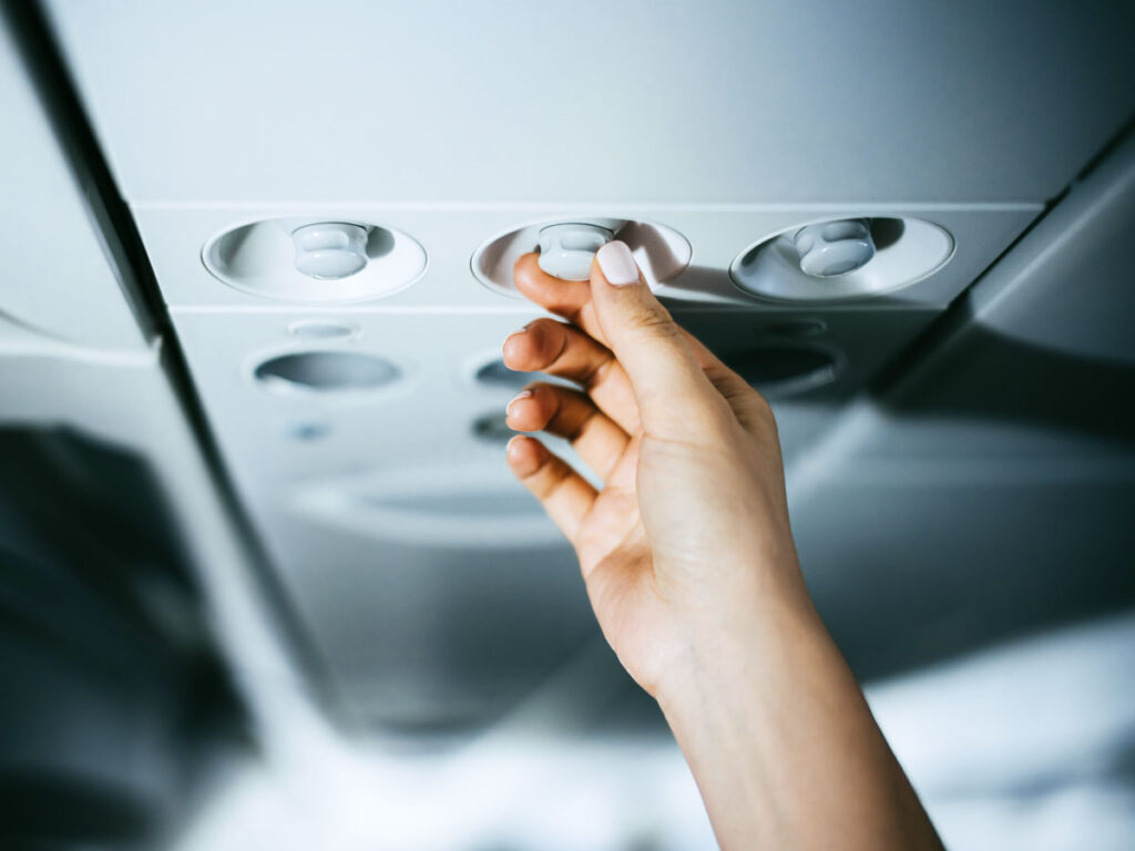 Traveler adjusting overhead air nozzle on airplane