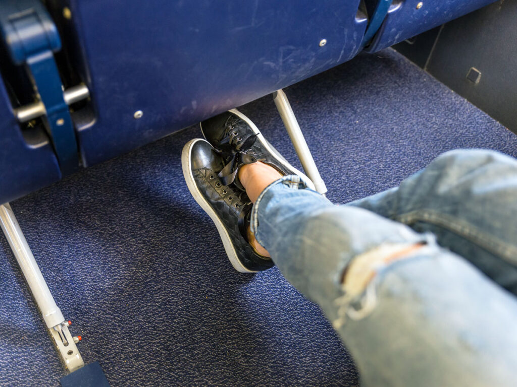 Airline passenger tucking shoes underneath seat in front